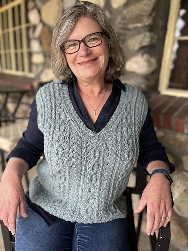 Smiling person wearing a grey cabled knit vests